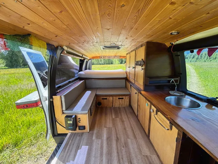 Wooden paneled RV rental interior featuring a cozy bed, kitchenette, and bench seating. Ready for adventures.. Ford Ford E350 1996