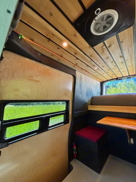 Custom RV rental interior. Wood ceiling, built-in bed, work table, and window offer a cozy mobile living space.. Nissan PRIMASTAR 2019