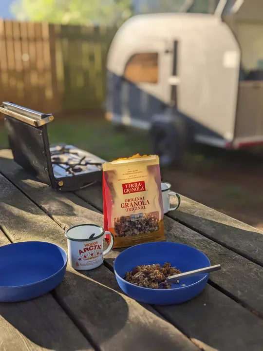 Camping breakfast featuring Terra Granola and coffee on a picnic table, next to a stove and an RV rental.. DROPLET 58 2026