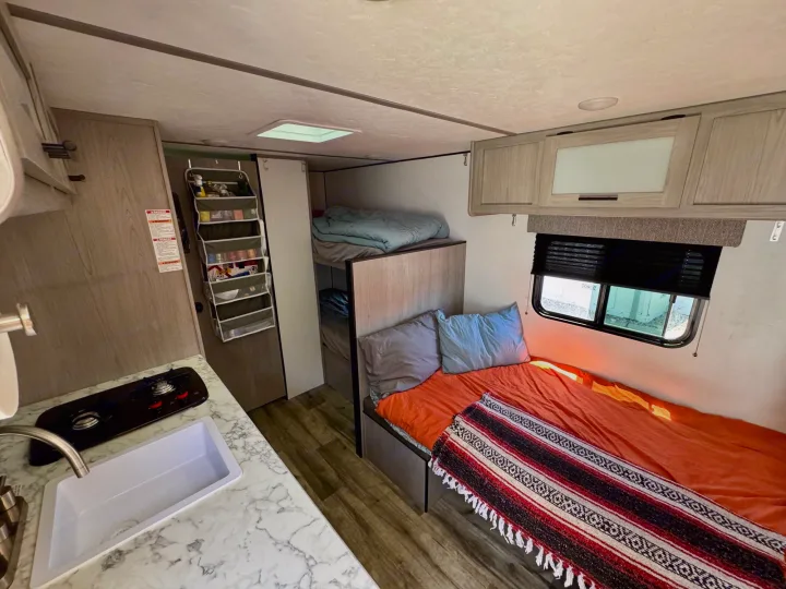 RV rental interior: A compact kitchen, bunk beds, and a comfortable main sleeping area with an orange blanket.. Coleman Lantern 17B 2024