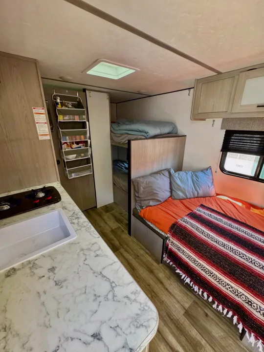 Cozy RV rental interior featuring a compact kitchen, main bed, and bunk beds, offering a complete living space.. Coleman Lantern 17B 2024