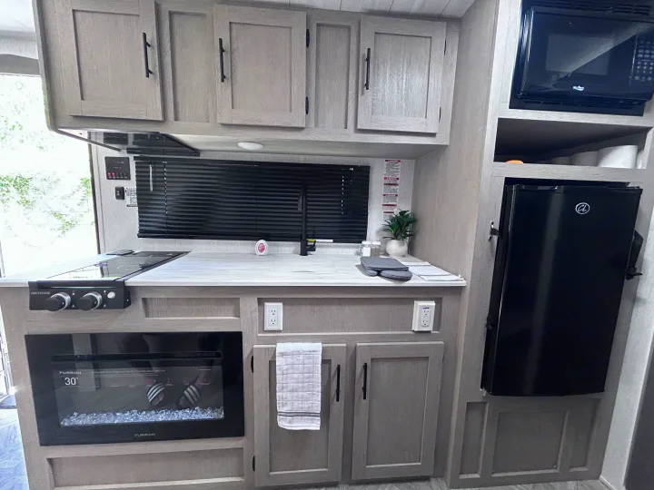 Step inside this RV rental's compact kitchen, featuring a Greystone cooktop, Furrion fireplace, microwave, and mini-fridge.. Forest River Salem Cruise Lite 2024