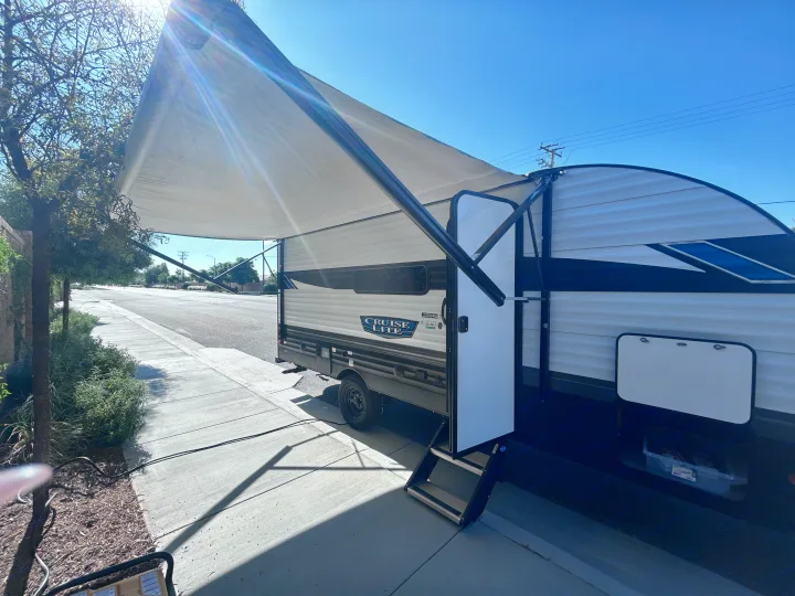 A white travel trailer RV rental with its large awning deployed, parked on a sunny day. Steps are out.. Forest River Salem Cruise Lite 2024