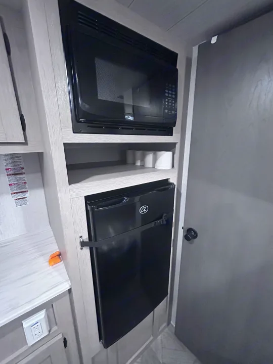 **rv rental** interior: compact kitchen area with a built-in microwave, mini-fridge, and shelf storage, next to a door.. Forest River Salem Cruise Lite 2024
