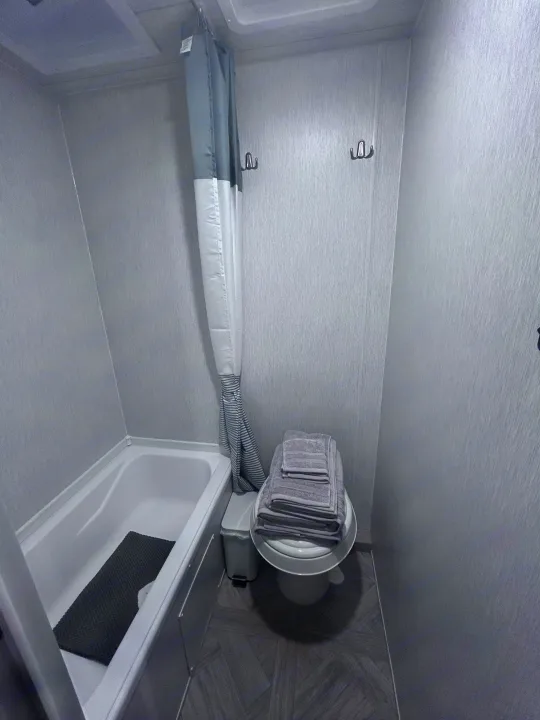 Clean, compact bathroom inside an RV rental, featuring a bathtub, toilet with towels, shower curtain, and wall hooks.. Forest River Salem Cruise Lite 2024