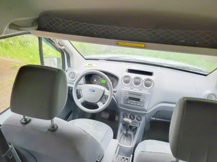 View inside an rv rental: the gray Ford van's dashboard, steering wheel, and overhead storage net from the rear seats.. Ford Transit 2013