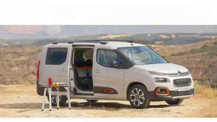 This light grey Citroën van, ideal for an RV rental adventure, is parked on dirt with its side door open and a table setup.. citroen Berlingo 2019