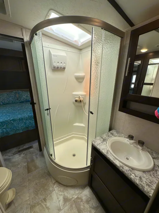 RV rental bathroom: bright shower, sink vanity, & a peek into the cozy bedroom.. Forest River Surveyor 2018