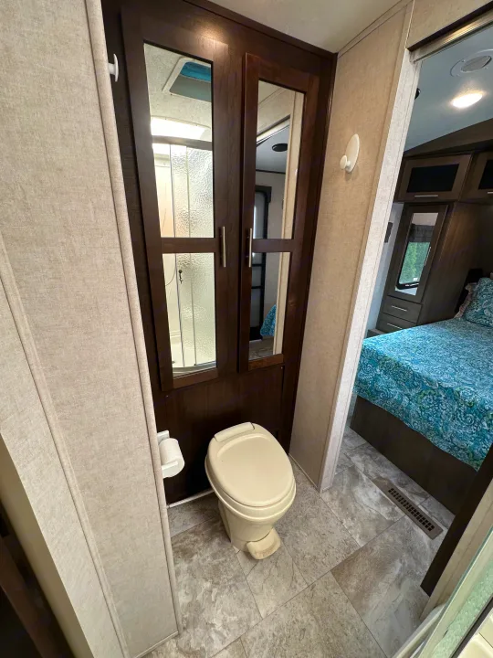 Inside an RV rental, a compact bathroom features a toilet and shower, leading to a comfortable bedroom.. Forest River Surveyor 2018