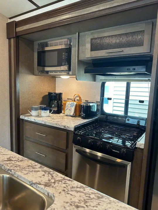 Inside an RV rental, this compact kitchen offers a microwave, stove, coffee maker, and ample counter space for travel.. Forest River Surveyor 2018