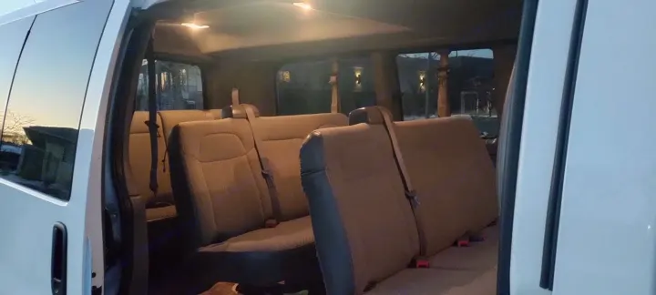 Interior of an RV rental van with multiple rows of tan passenger seats visible through the open side door. Overhead lights illuminate the cabin.. Chevrolet Express 2016