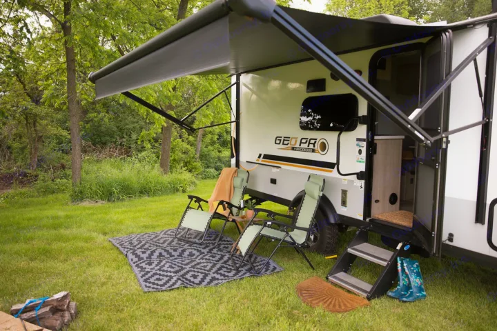 Experience outdoor leisure with this rv rental! Camper set up with awning, chairs, steps, and mat in a serene, green setting.. Forest River Rockwood Geo Pro 2022