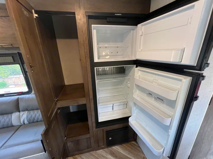 View of an RV rental's interior, highlighting an open Dometic refrigerator-freezer, adjacent storage cabinet, and sofa.. Forest River EVO 208RD 2021