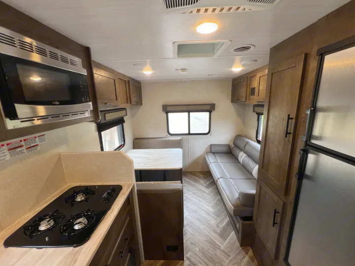 Inside this RV rental, find a compact kitchen with a microwave and stovetop, a cozy dinette, and a comfy sofa.. Forest River EVO 208RD 2021
