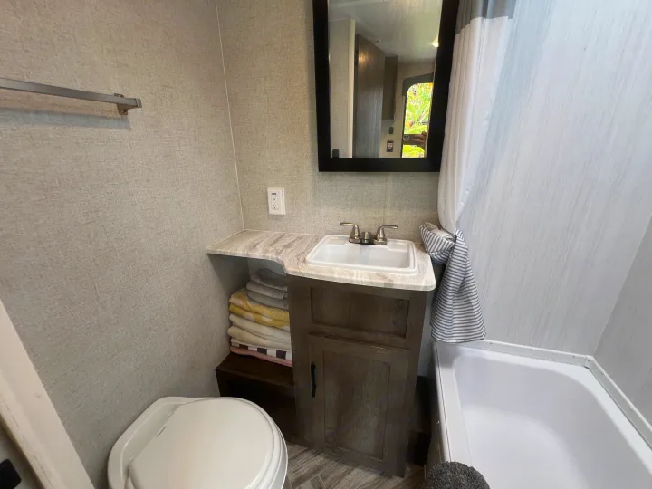 Compact & modern RV rental bathroom features a sink, mirror, toilet, shower, and towel storage.. Forest River EVO 208RD 2021