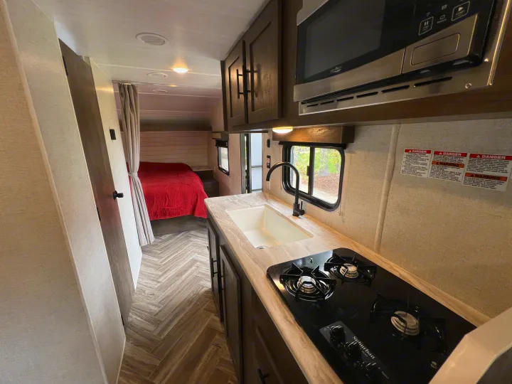 Modern RV rental interior: a sleek kitchen with sink, stovetop, and microwave, opens to a cozy bedroom.. Forest River EVO 208RD 2021