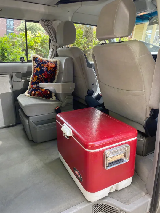 Cozy RV rental van interior with comfortable gray seats, a floral pillow, and a red Coleman cooler.. Volkswagen Westfalia 2003