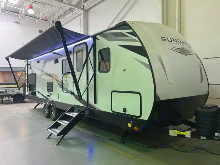 Brightly lit Sundance travel trailer for rv rental. Features an extended awning, steps, and stylish two-tone exterior.. Heartland Sundance 2024