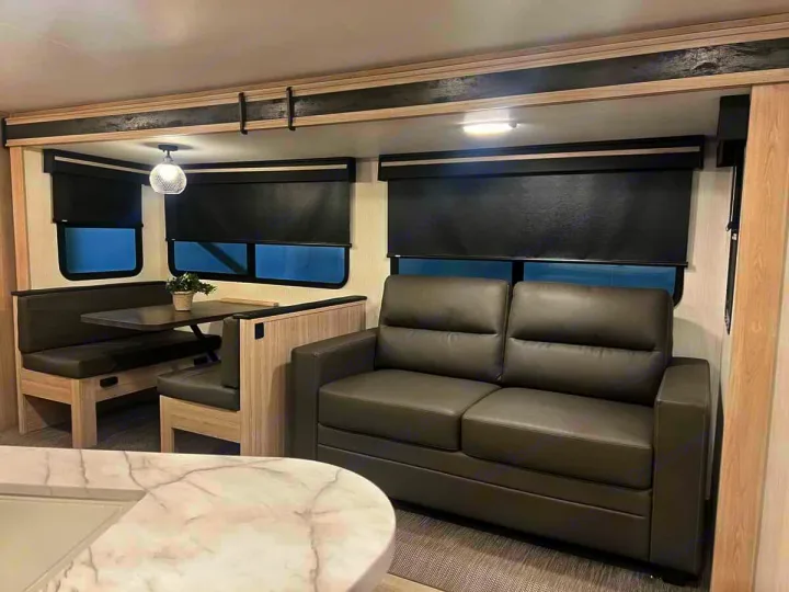 Modern rv rental interior with a dark gray booth dinette, matching sofa, and a light marble-pattern kitchen counter.. Heartland Sundance 2024