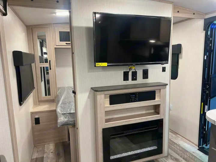Bright rv rental interior with wall TV, media console, electric fireplace, and a compact bunk bed.. Heartland Sundance 2024