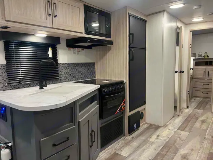 Inside your RV rental: a modern, well-equipped kitchen featuring a sink, stove, fridge, and stylish finishes.. Heartland Sundance 2024