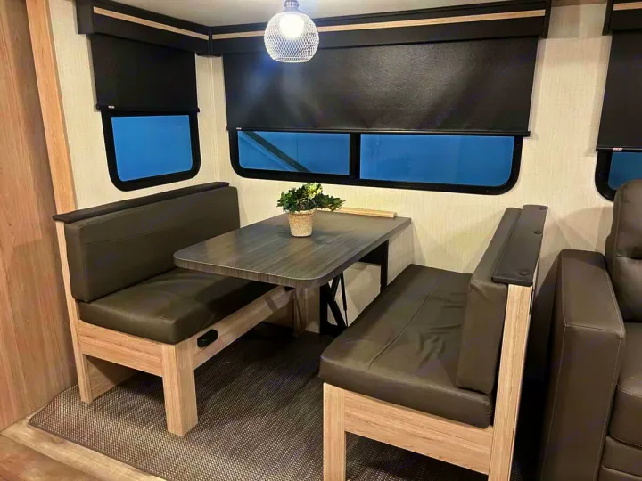 Inside this RV rental, a compact dinette offers dark grey bench seating and a table, perfect for meals and activities.. Heartland Sundance 2024