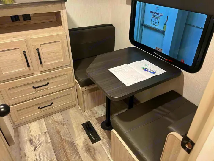 RV rental: Cozy dinette with a coloring book, adjacent storage cabinets, and a window showing an emergency exit.. Heartland Sundance 2024