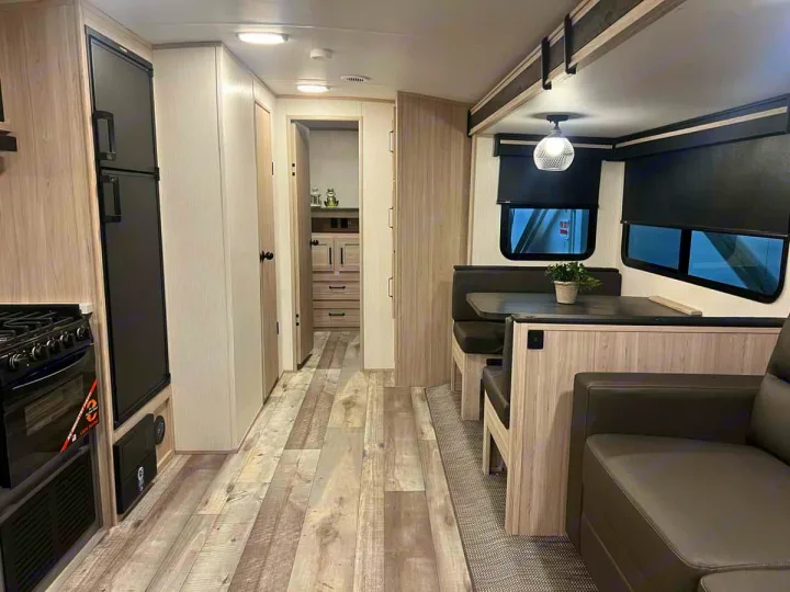 Explore this modern RV rental interior featuring light wood, black appliances, a comfortable dinette, and sofa. Perfect for travel.. Heartland Sundance 2024