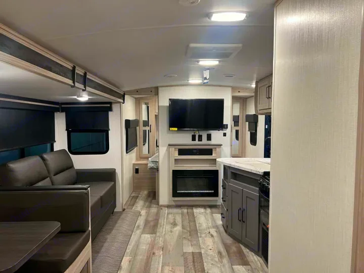 Modern RV rental interior with a living room, kitchen island, TV, fireplace, and wood-look flooring.. Heartland Sundance 2024