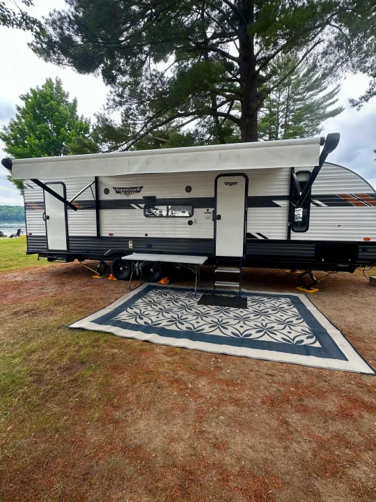 Spacious RV rental set up at a lakeside campsite with an outdoor rug & extended awning, perfect for a relaxing getaway.. Forest River Wildwood X-Lite 2021