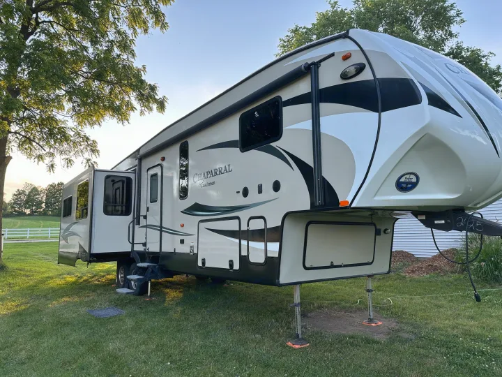 A beige and black Chaparral fifth-wheel RV rental with slide-outs extended, set up on grass. Ideal for camping.. Forest River Coachmen Chapparal 2016