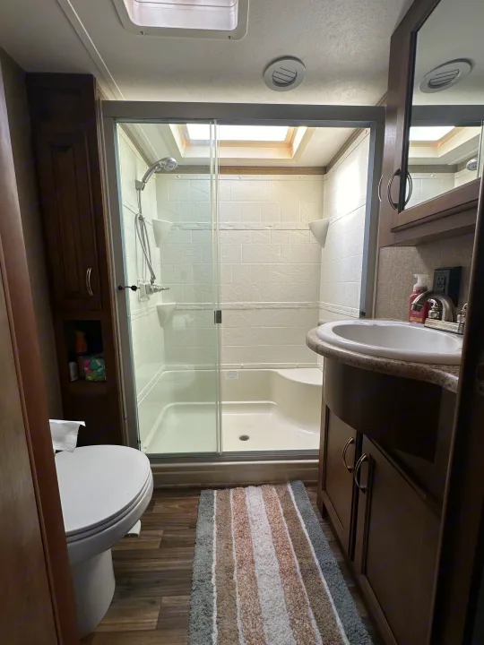 A well-lit, compact RV rental bathroom featuring a glass shower, overhead skylight, toilet, and vanity sink.. Forest River Coachmen Chapparal 2016