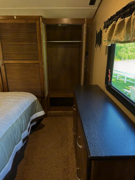 Inside an RV rental bedroom: features a comfortable bed, open closet, and dresser. Window offers outdoor view.. Forest River Coachmen Chapparal 2016