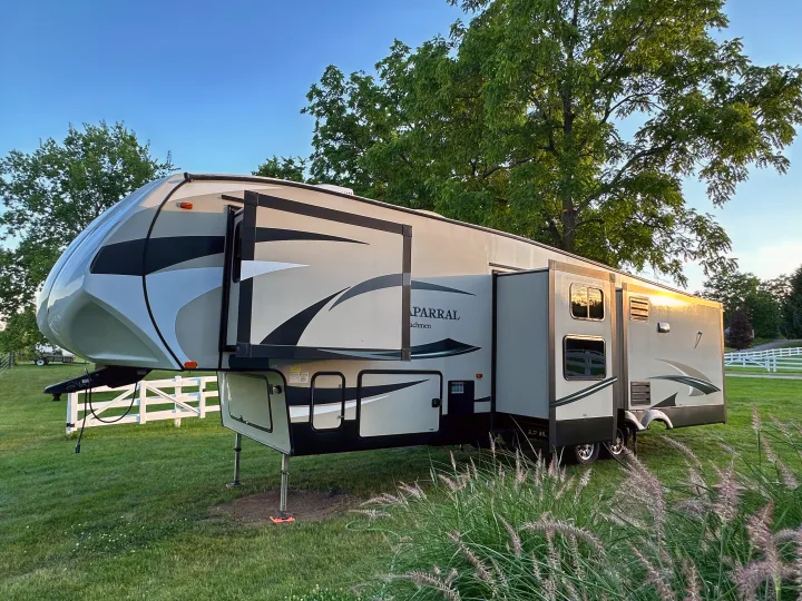 Modern fifth-wheel RV rental parked in a grassy campsite with extended slide-outs, ready for a comfortable outdoor vacation.. Forest River Coachmen Chapparal 2016