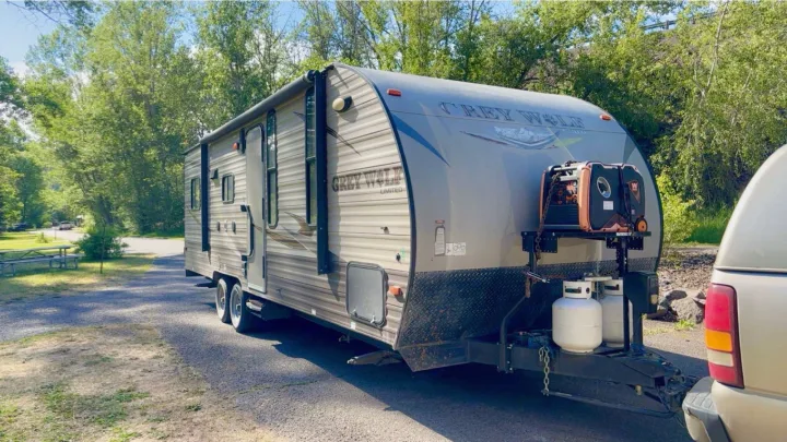 Grey Wolf travel trailer, equipped with generator & propane tanks, parked at a scenic, treed campsite. Ideal RV rental.. Forest River Cherokee Grey Wolf Toy Hauler 2016