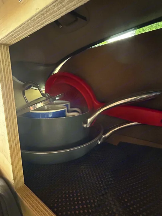 Organized kitchen essentials in an RV rental: nesting pots, pans, mugs & a red colander. Perfect for campervan cooking.. Dodge Caravan 2003
