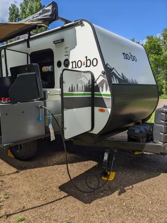 Side view of a white Forest River No Boundaries RV rental camper with an open outdoor kitchen and awning.. Forest River 10.6 no boundaries 2022