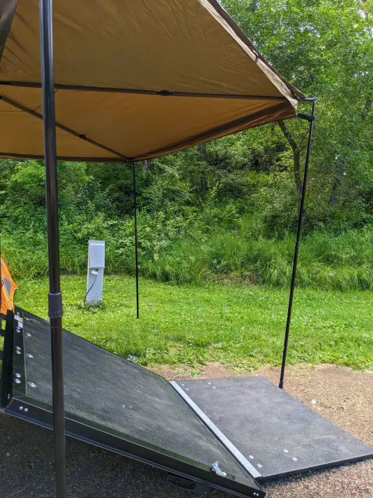 RV rental site setup: canopy, accessible ramp, and utility hookup in a green camping area.. Forest River 10.6 no boundaries 2022