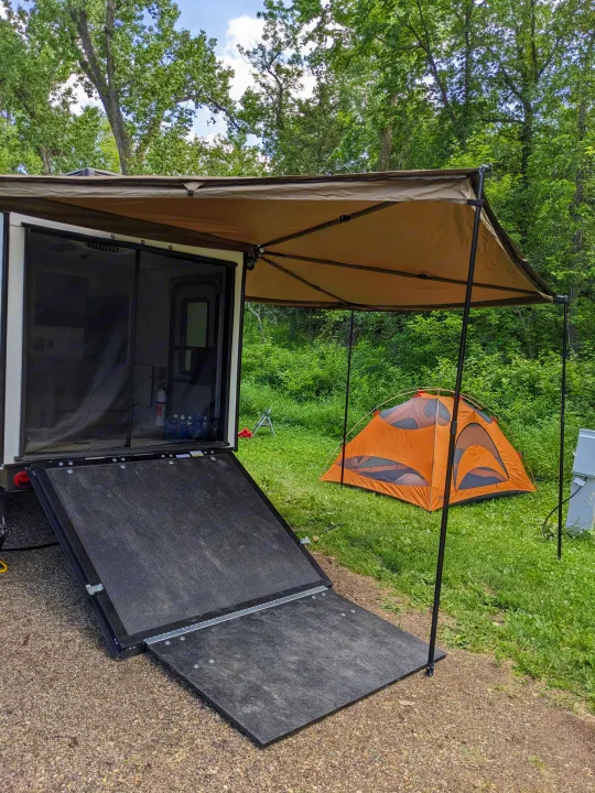An RV rental with a large tan awning, open ramp, and an orange tent on green grass. Perfect for outdoor camping.. Forest River 10.6 no boundaries 2022