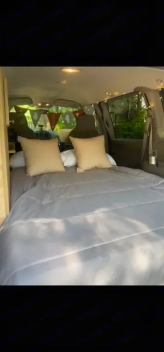 Cozy RV rental van interior with a bed, light pillows, and string lights, ready for your next adventure.. Dodge Caravan 2003