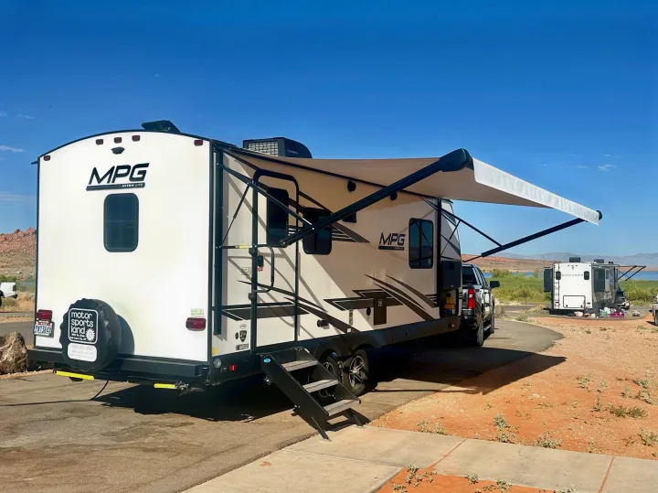 An MPG Ultra-Lite RV rental with its awning extended, parked at a sunny campground near water, ideal for road trips.. Cruiser RV MPG Ultra Lite 2022