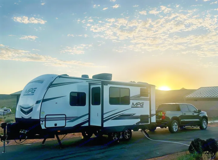 Travel trailer RV rental and truck under a vibrant sunset sky at a camp spot. Ready for your next outdoor adventure!. Cruiser RV MPG Ultra Lite 2022