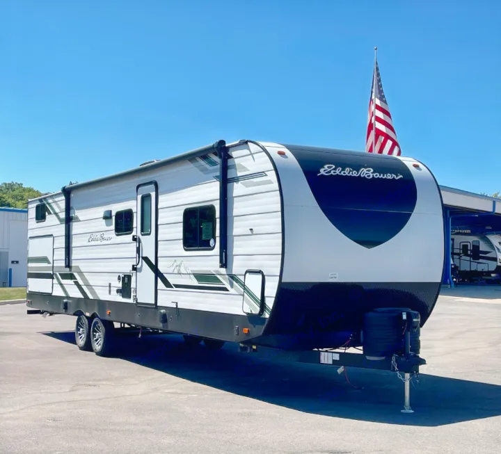 An Eddie Bauer travel trailer, perfect for RV rental. This white camper features black & green graphics, parked on asphalt.. Keystone RV Eddie Bauer 34bsbh 2024