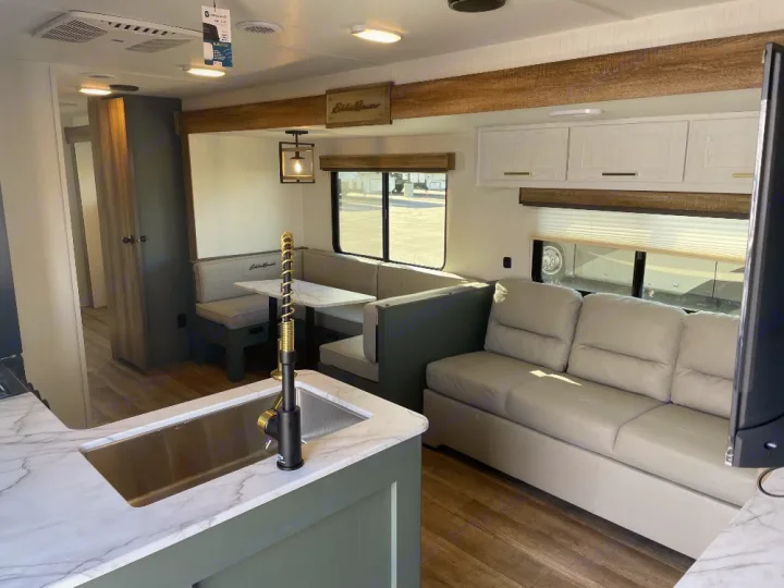 Bright, modern RV rental interior featuring a kitchen with sink, U-shaped dinette, and comfortable sofa.. Keystone RV Eddie Bauer 34bsbh 2024