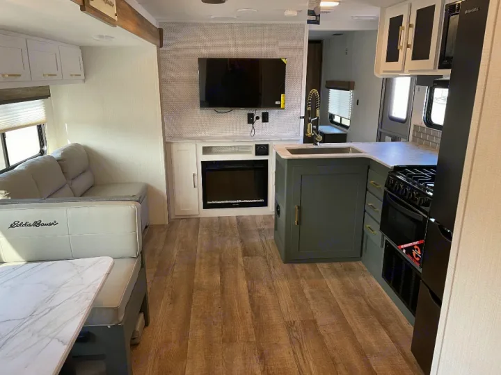 Modern RV rental interior: kitchen with sink/stove, dinette, sofa, TV, and fireplace. Ideal for road trips.. Keystone RV Eddie Bauer 34bsbh 2024