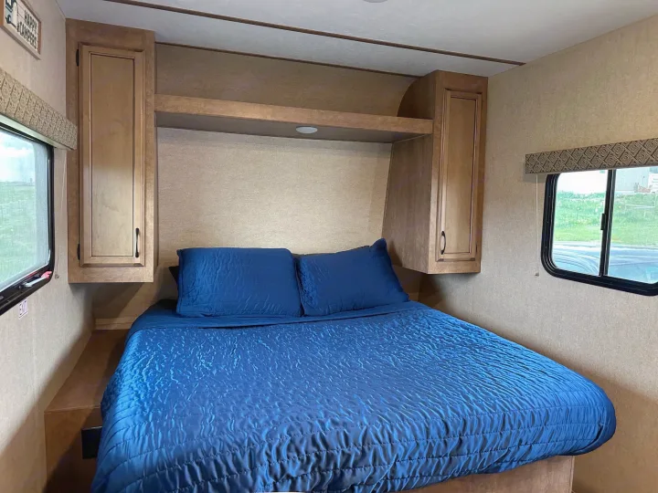 Cozy RV rental bedroom featuring a blue bed, overhead cabinets, and side windows.. Starcraft Launch Outfitter Extreme 2018