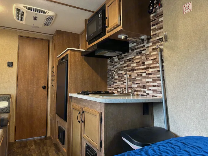 Explore this RV rental's cozy interior, featuring a compact kitchen with microwave, fridge, and stovetop, plus a comfortable bed.. Starcraft Launch Outfitter Extreme 2018