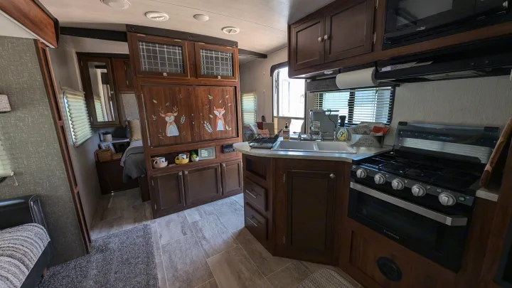Cozy RV rental interior: wood-paneled kitchen with sink & stove, plus bedroom and living area, for compact travel.. Heartland RVs Mallard 2019