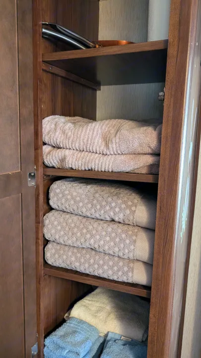 Inside an RV rental cabinet: neatly folded towels (beige, blue) & kitchen tongs. Essential storage for your travels.. Heartland RVs Mallard 2019