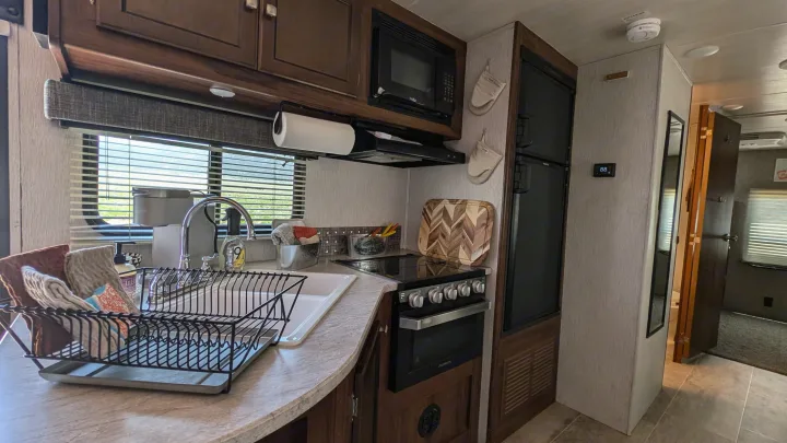 Kitchen in an RV rental, featuring a full stove, microwave, fridge, and sink for comfortable travel.. Heartland RVs Mallard 2019